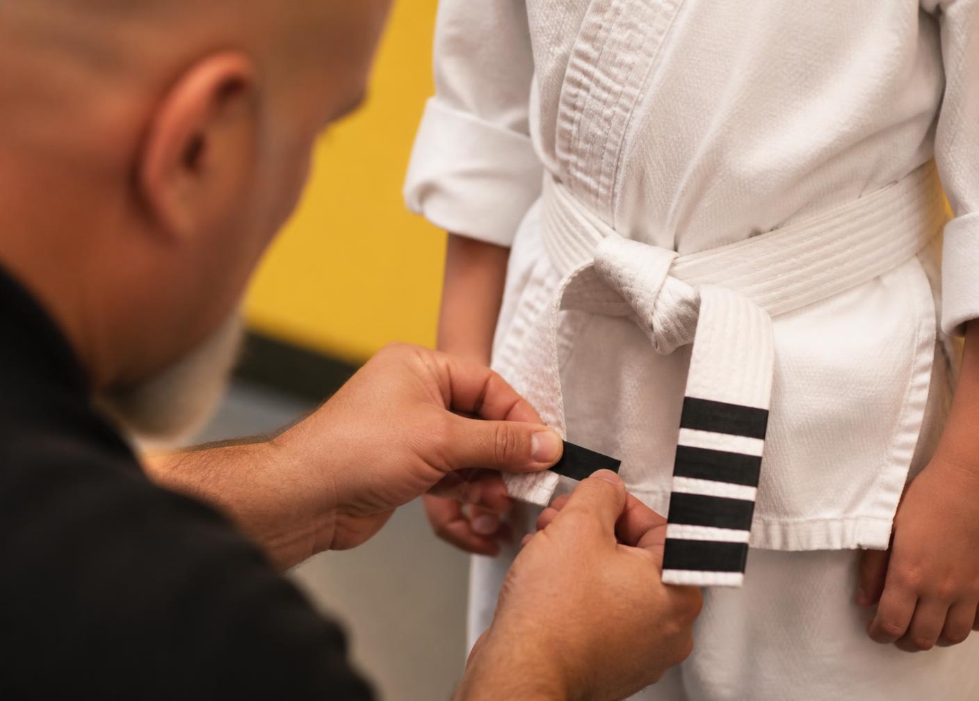 Instructor placing a new stripe on a student's white belt at Pride Martial Arts